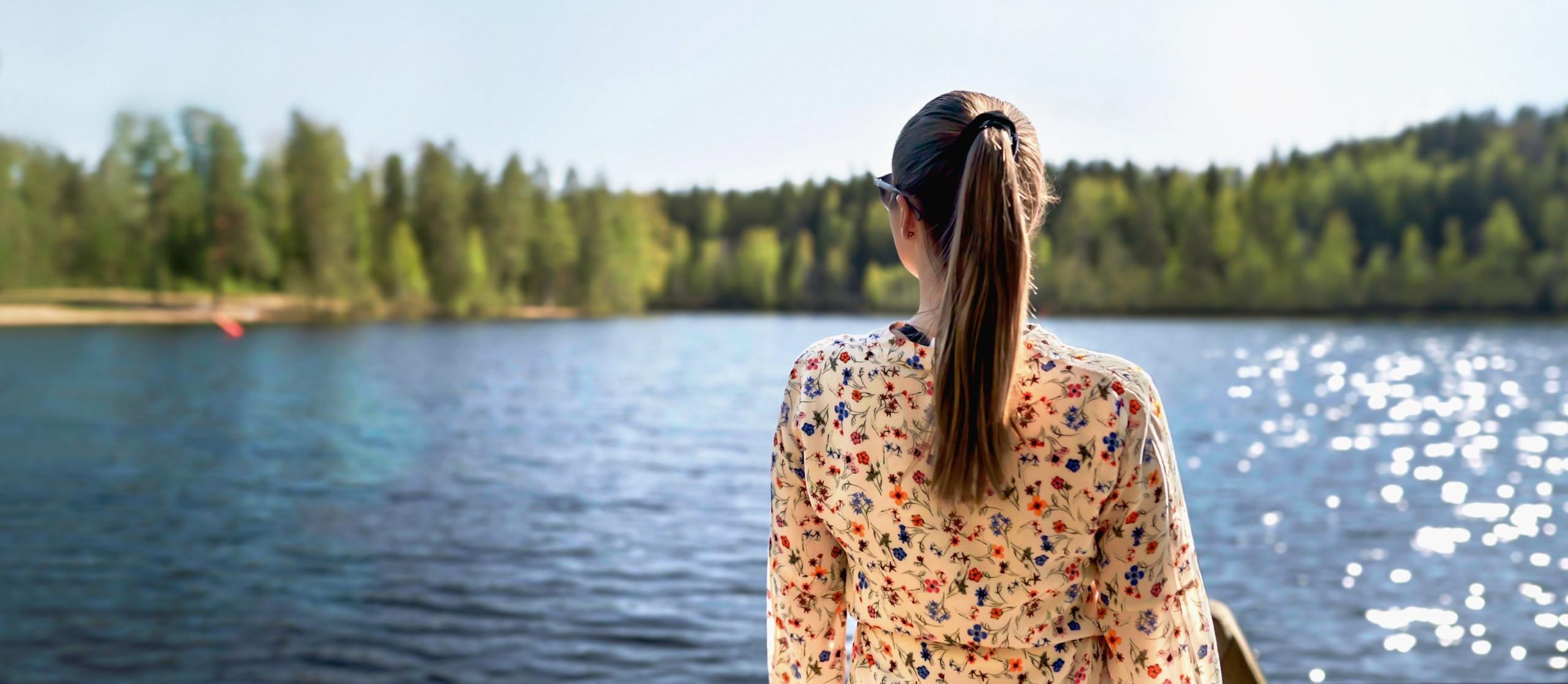 Nuori nainen katsoo suomalaista järvimaisemaa selin kuvaajaan